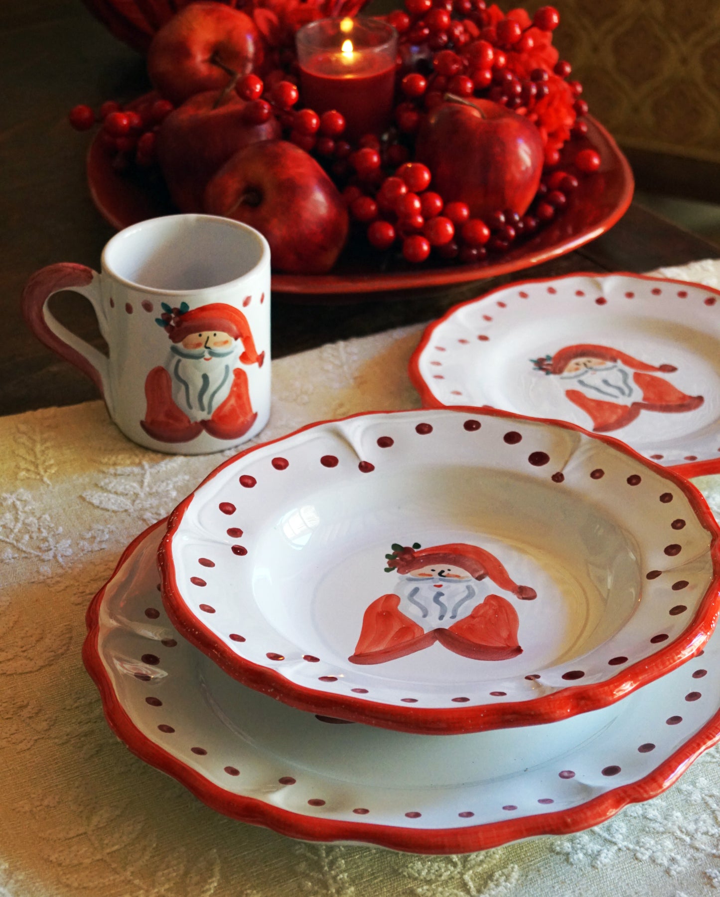 Christmas-themed tableware with Santa Claus design on plates and a mug on a table with berries and a candle.