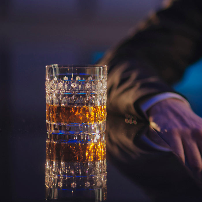 Glass of whiskey on a bar with a person in a suit in the background