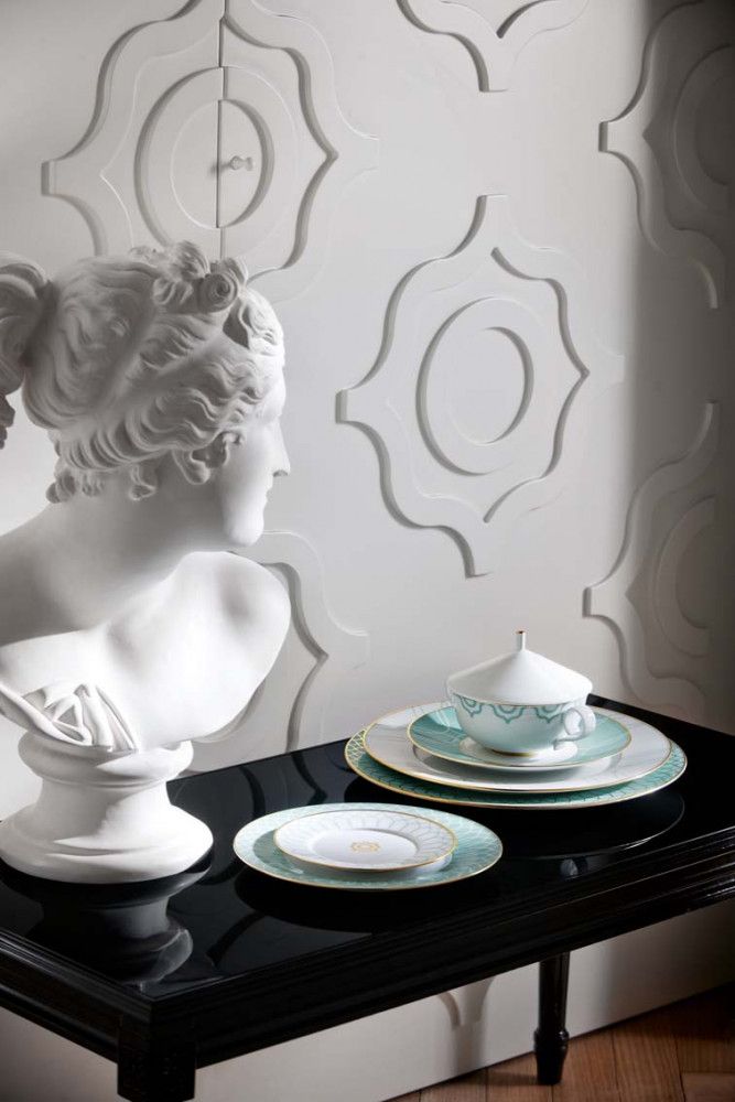 Porcelain dinnerware with green pattern on a black wood table against an ornate white wall.