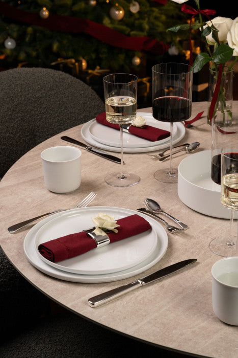 Dining table set for a festive meal with red napkins, wine glasses, and a Christmas tree in the background.