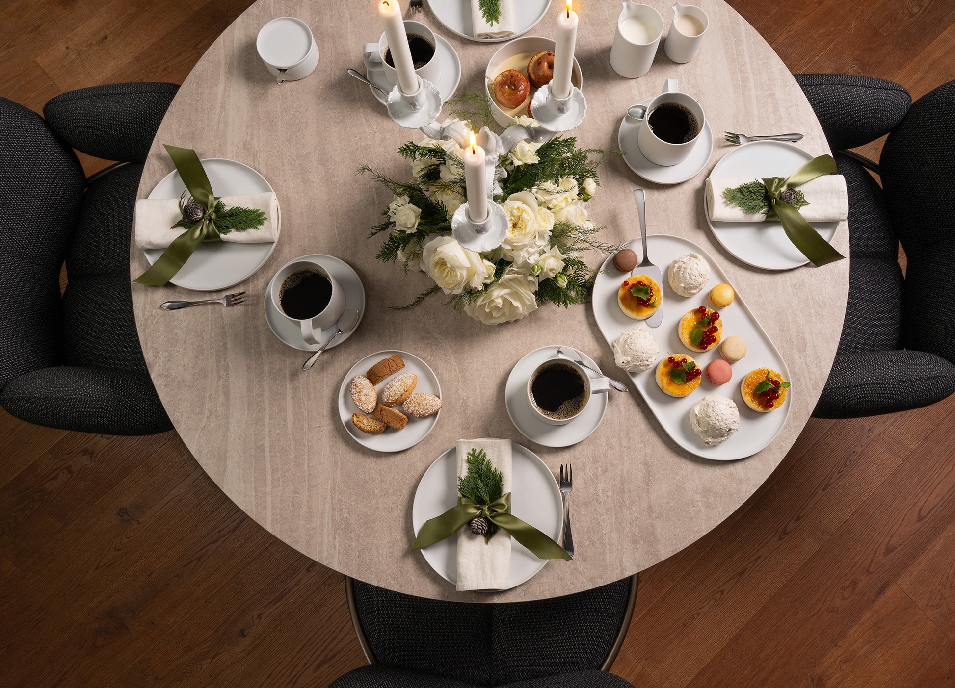 Round table set for a meal with white plates, cups, and a centerpiece on a wooden floor.