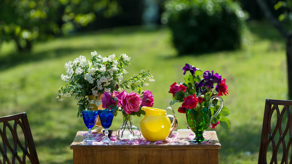 Table with floral arrangements and a yellow pitcher on a grassy outdoor setting