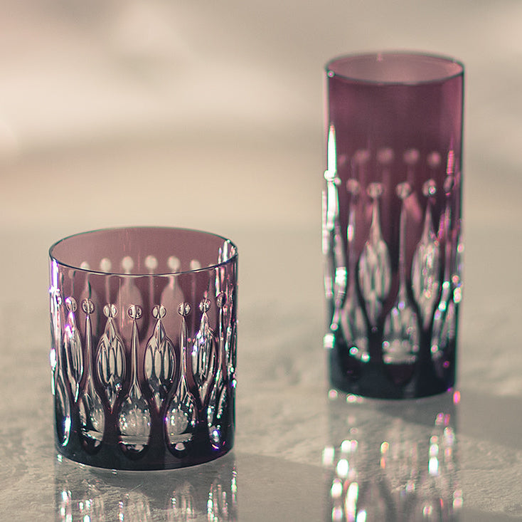Two purple glass tumblers on a reflective surface with a blurred background