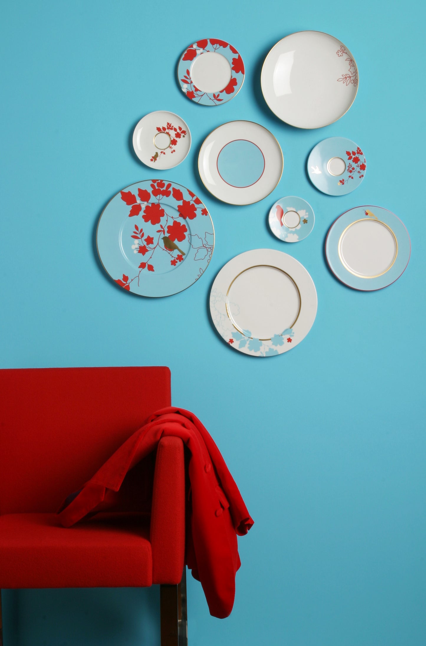 Decorative plates with floral patterns on a blue wall above a red chair.