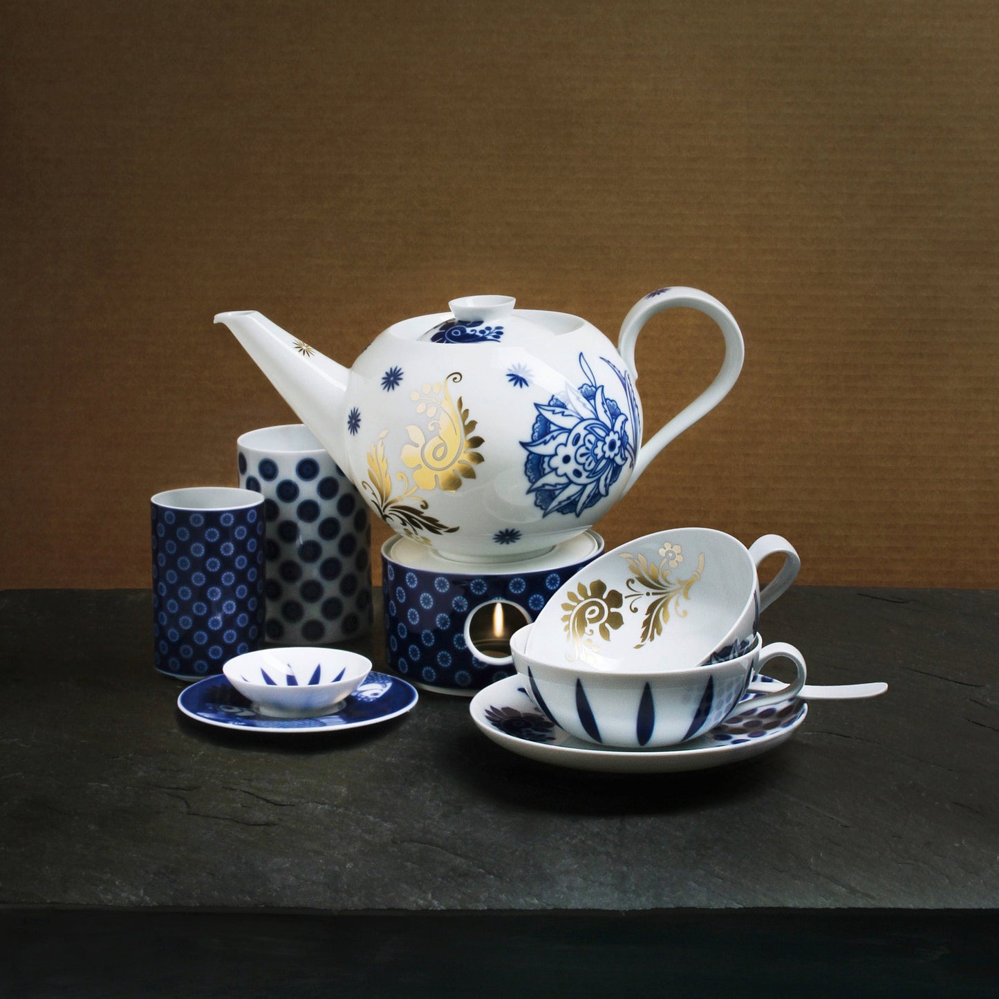Ceramic teapot and cups with blue and white patterns on a dark surface.