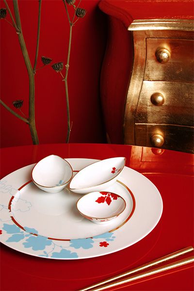 Decorative table setting with a plate and small floral bowls on a red surface.