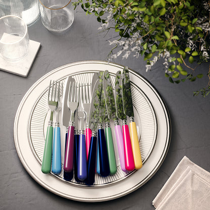 Set of colorful cutlery handmade in France on a round plate with a gray background