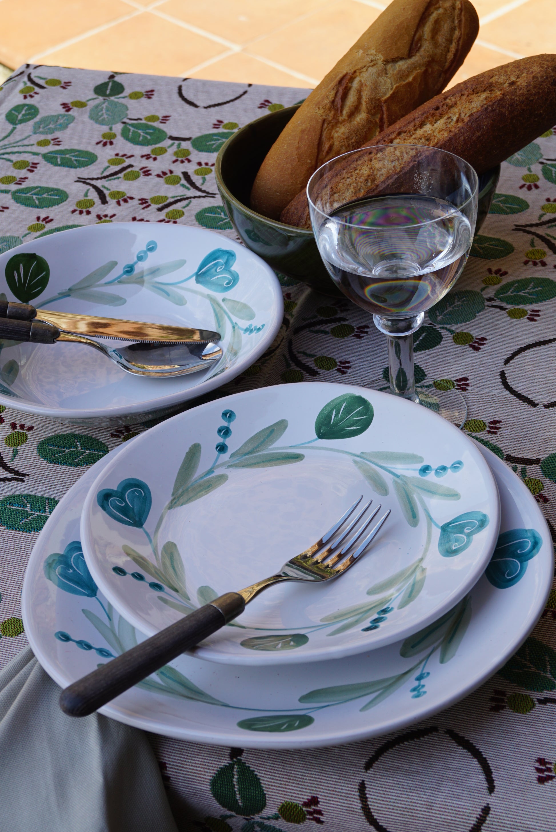 Set of white ceramic plates with blue and green floral patterns on a patterned tablecloth.