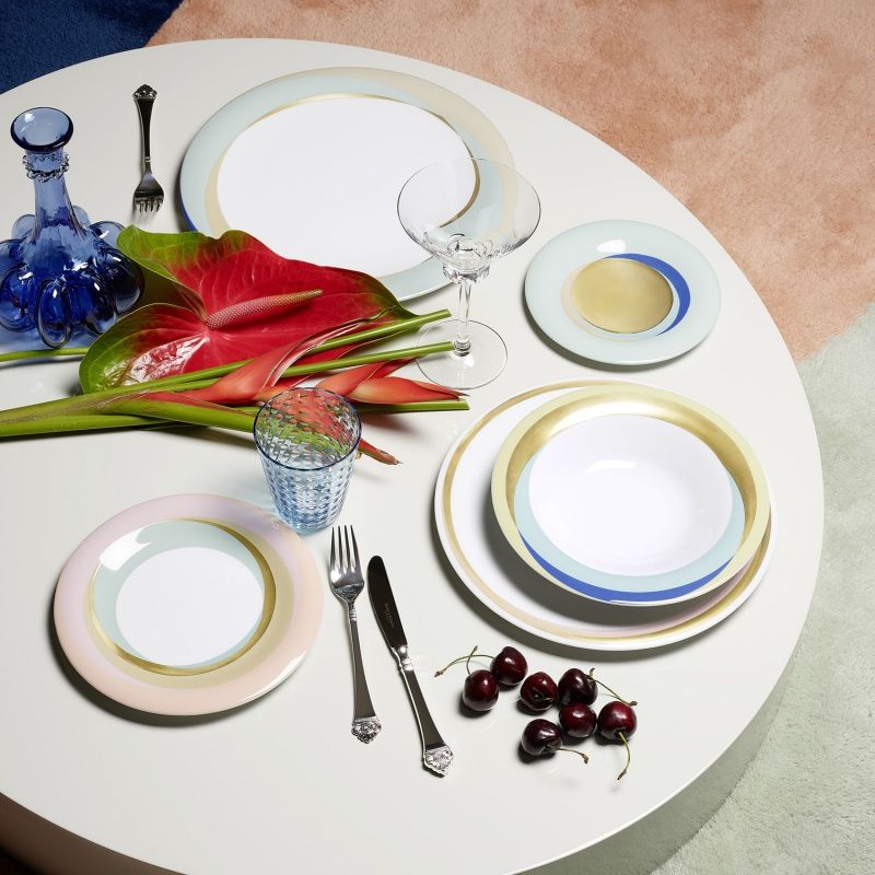 Dining table setting with colorful pastel plates, glasses, and cutlery on a white surface.