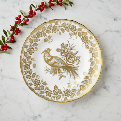 Decorative plate with gold floral and bird design on a marble surface with holly berries.