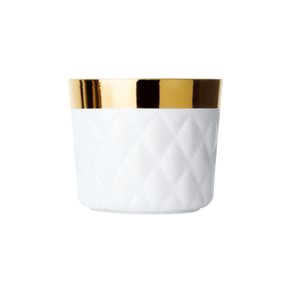 A white porcelain champagne tumbler with a quilted texture and a gold rim and interior, against a plain background.