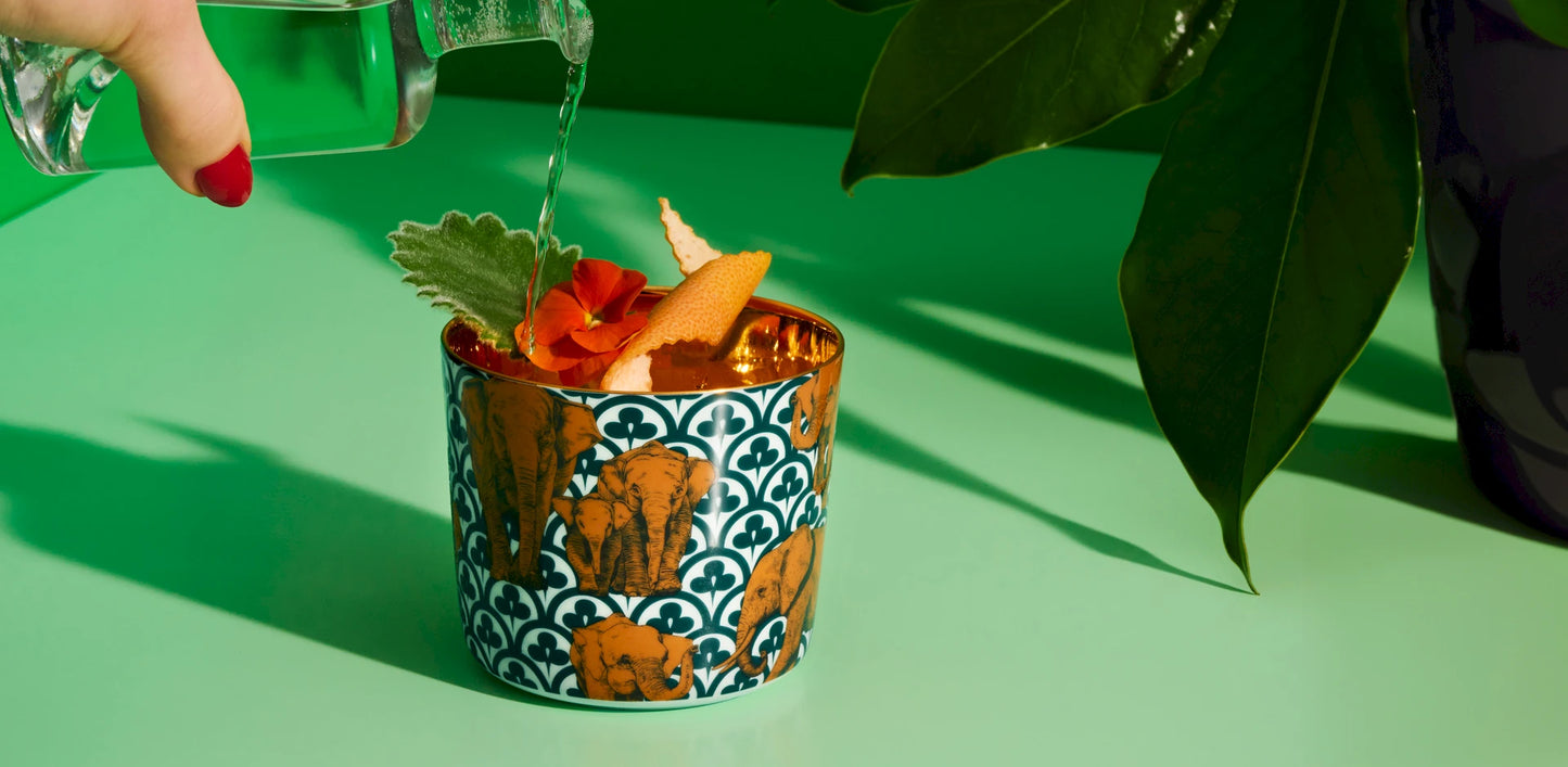 Porcelain champagne tumbler with elephant design being filled with a cocktail reflecting off the gold interior