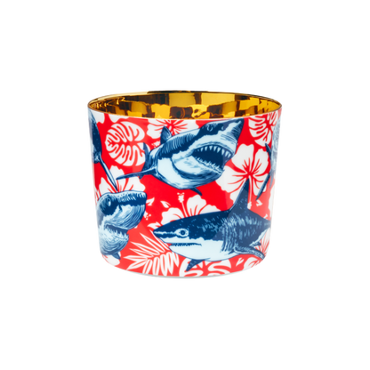 A multicolored porcelain champagne tumbler with a gold interior, decorated with blue sharks against a red patterned background.