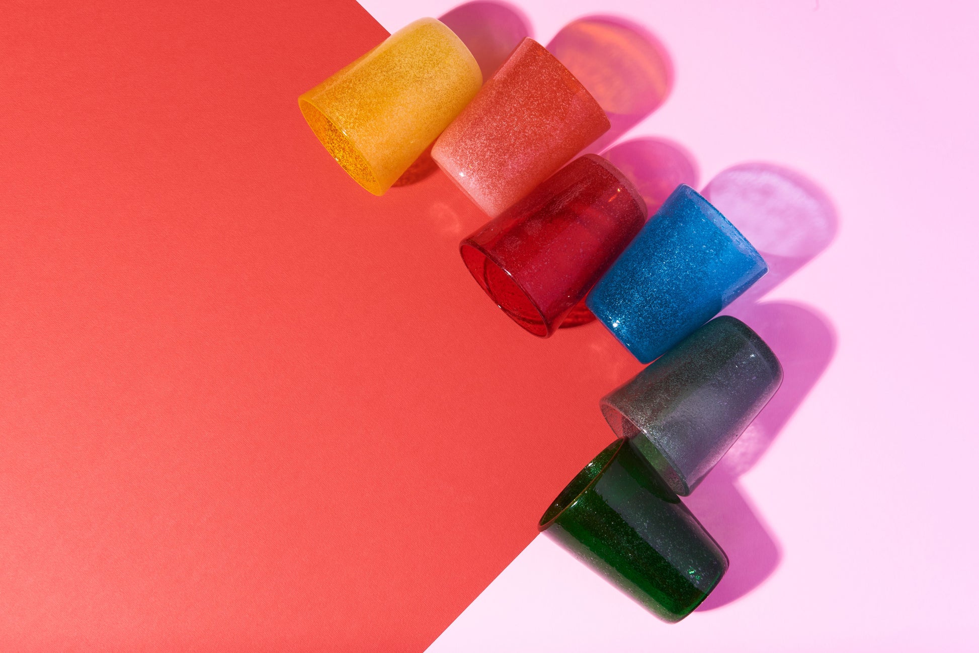 Colorful glass tumblers on a pink and red background