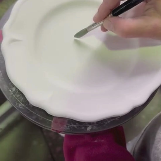 Ceramic white plate being glazed by hand with a blue floral pattern