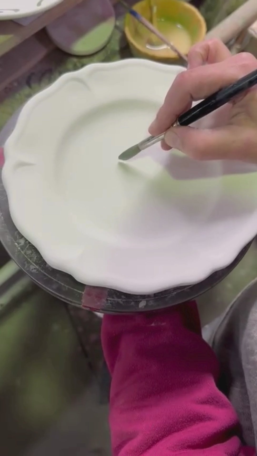 Ceramic white plate being glazed by hand with a blue floral pattern