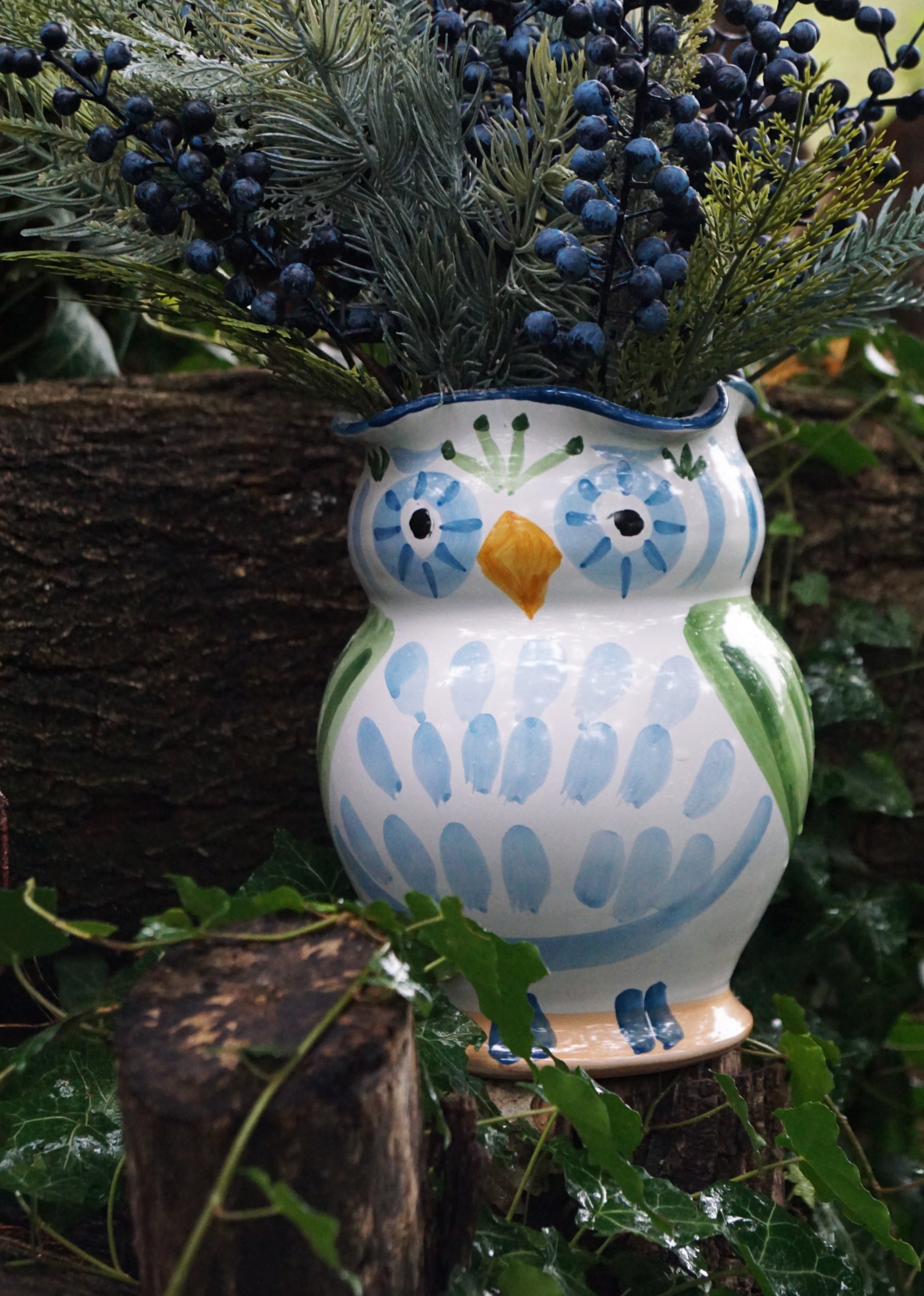 Ceramic owl vase with blue and green design, filled with plants, on a natural background.
