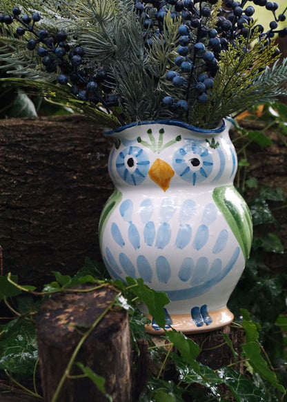 Ceramic owl vase with blue and green design, filled with plants, on a natural background.